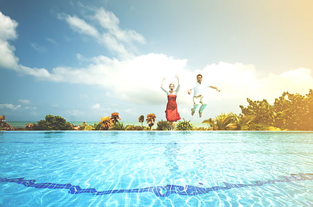 man and woman jumping on pool during daytime