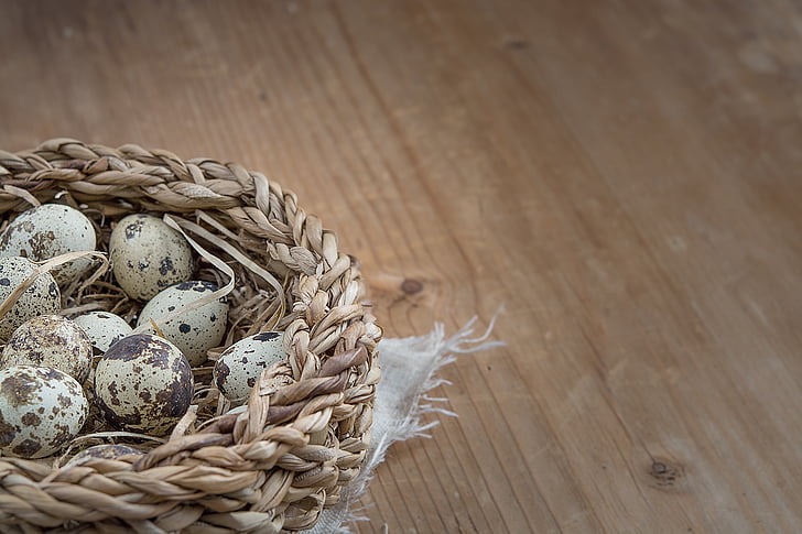 clutch of quail eggs in basket on brown wooden surface