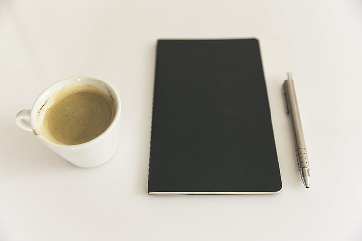 black notebook beside mug and pen