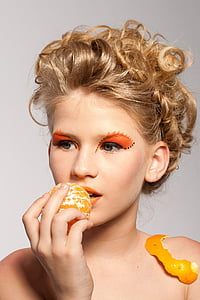woman with orange eyeshadow holding peeled orange fruit