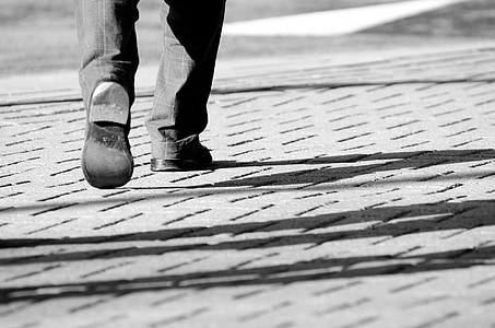 person wearing pair of black shoes while walking on gray pavement