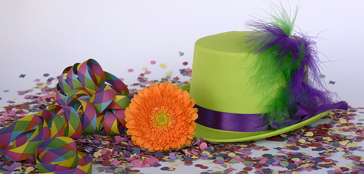 green and purple hat beside orange flower on top of confetti