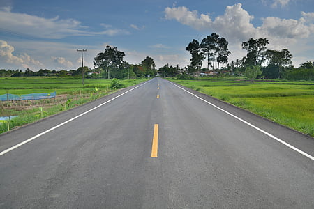 gray asphalt road between green grass field at daytime