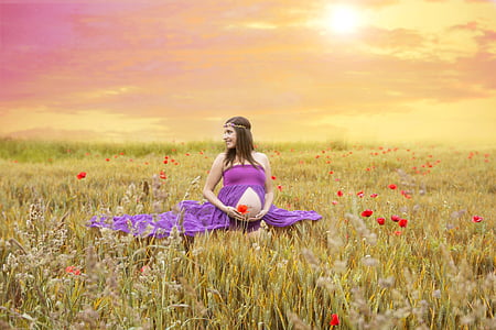 pregnant woman in purple dress sitting on green grass field during daytime