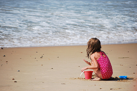 girl in pink and white polka-dot sleeveless onepiece playing on shoreline beside sea