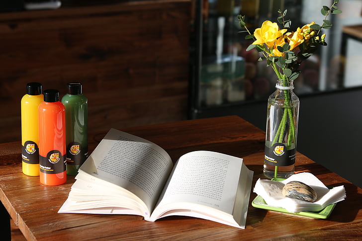 open book on top of table beside flower vase with yellow roses