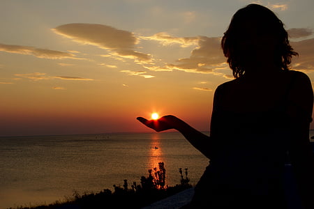 silhouette of forced perspective photography of woman facing sunset while sun on left hand
