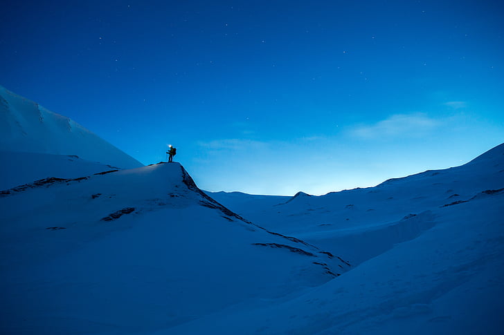 silhouette of man carrying backpack on snow filled mountain