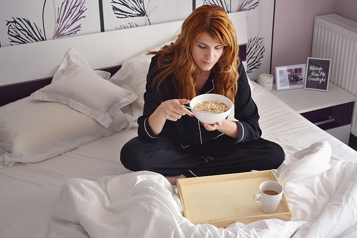 woman on bed eating cup of noodle