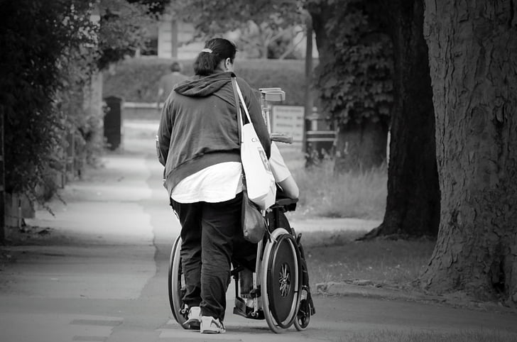 grayscale photography of woman pushing wheelchair