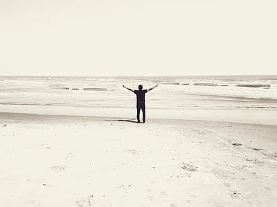 man rising hand standing on seashore at daytime