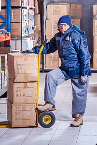 man wearing blue jacket beside yellow hand truck