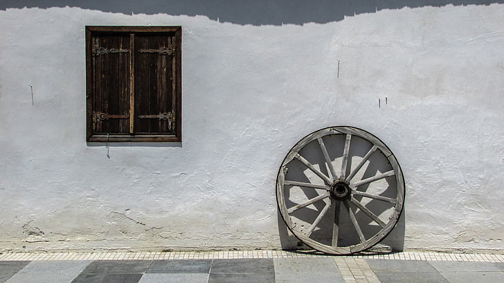 gray wooden wheel beside wall at daytime