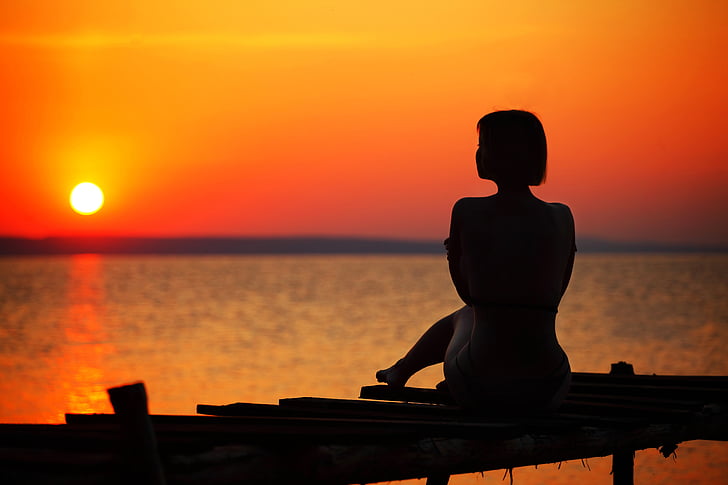 silhouette of woman sitting on dock during golden hour