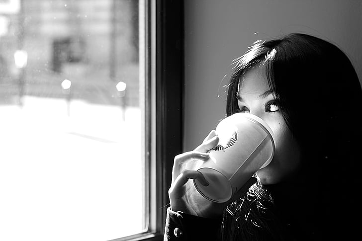 grayscale photography of woman drinking coffee near the mirror