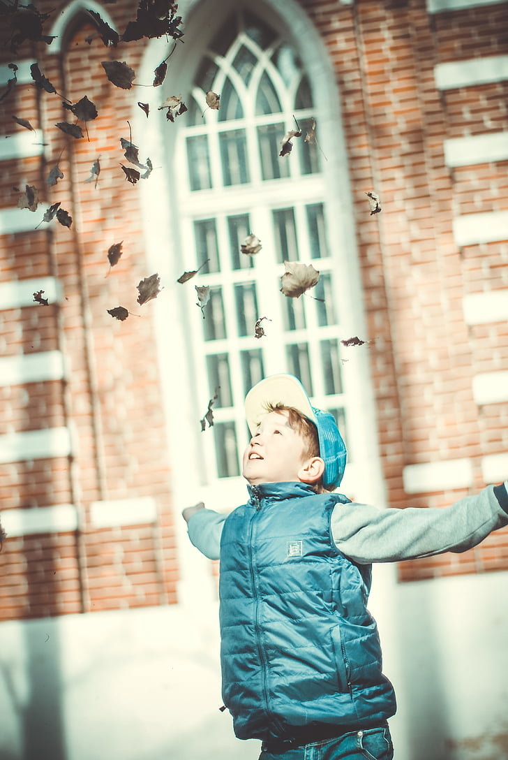 boy wearing blue zip-up vest throwing leaves on air