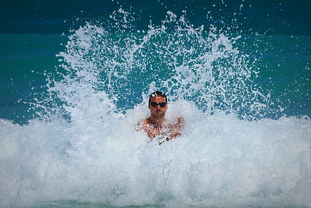 man wearing sunglasses standing between sea waves during daytime
