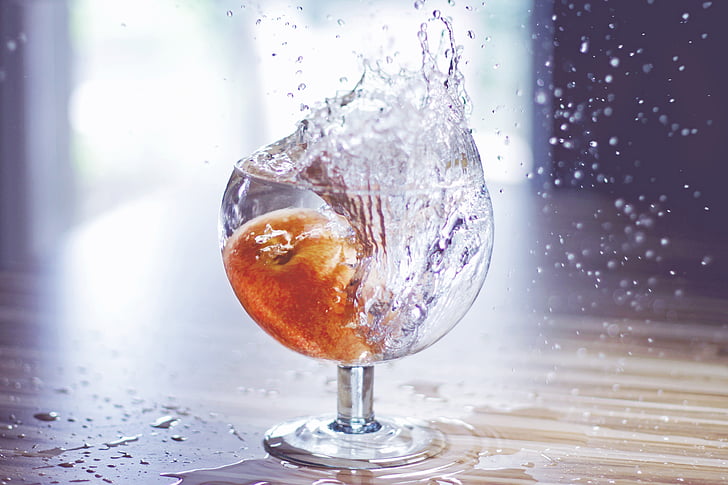 fruit drop on water filled drinking glass spilling water on brown surface