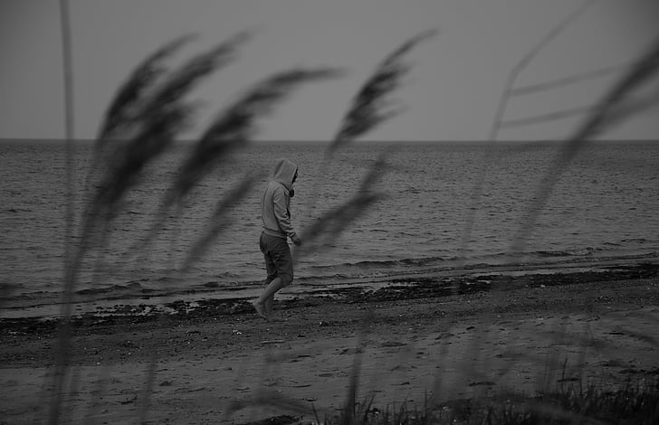 greyscale photo of person in hoodie walking in seashore