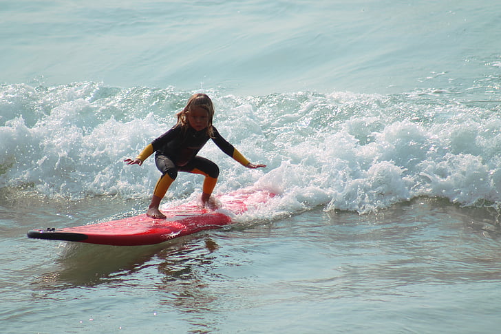 girl riding red surfboard in the ocean during daytime
