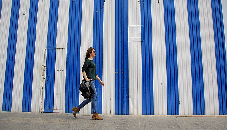 woman with green shirt and blue jeans and brown boots walking in the road during daytime