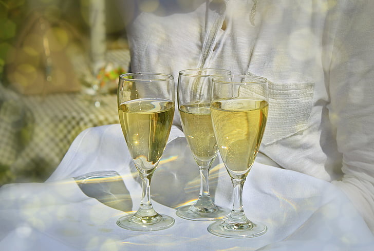 photo of three champagne glasses with champagne on white table cloth