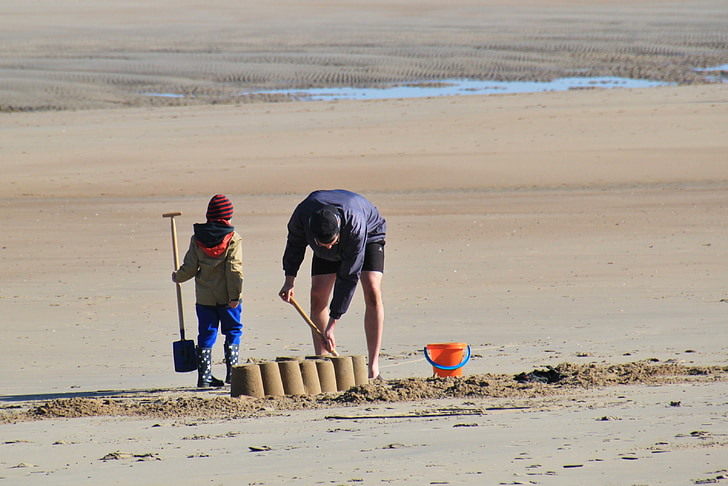 man and child making sand castles during daytime