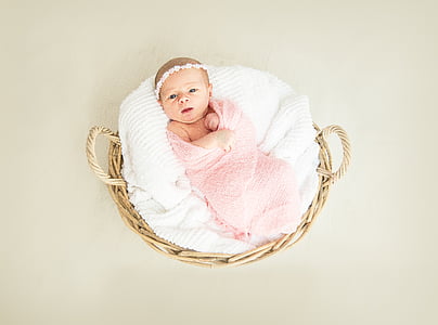 baby covered by pink swaddle on round brown wicker basket