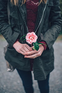 photography of woman in black jacket holding a pink flower