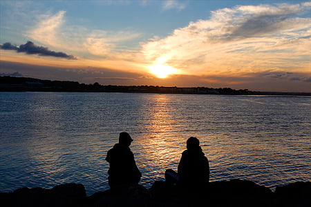 silhouette photo of two man sitting in front of body of water