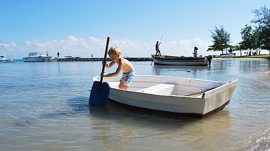 boy standing on white boat while holding blue paddle during daytime