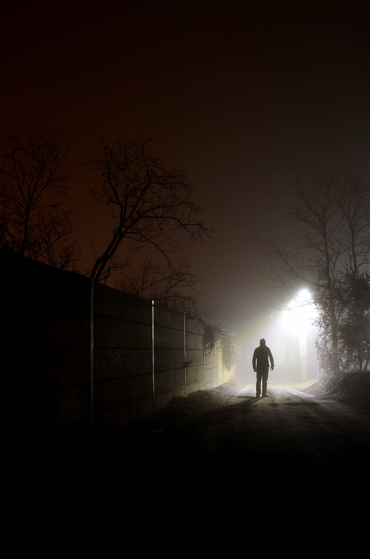 silhouette photography of man walking beside wall near street igh