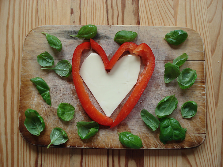 sliced red vegetable form heart and green leafs on brown wooden chopping board