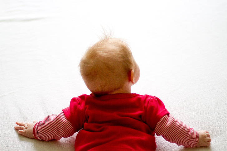 baby wearing red long-sleeved shirt laying on white surface