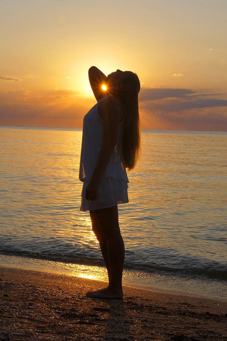 woman wearing white tank dress standing on seashore at sunset