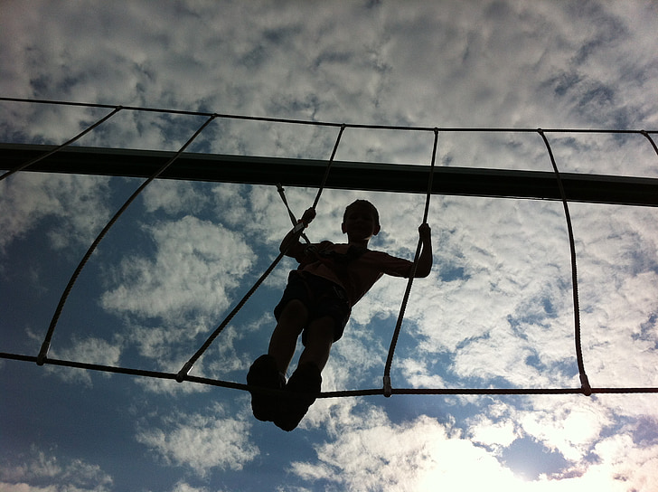 low angle photography of boy standing on hanging bridge