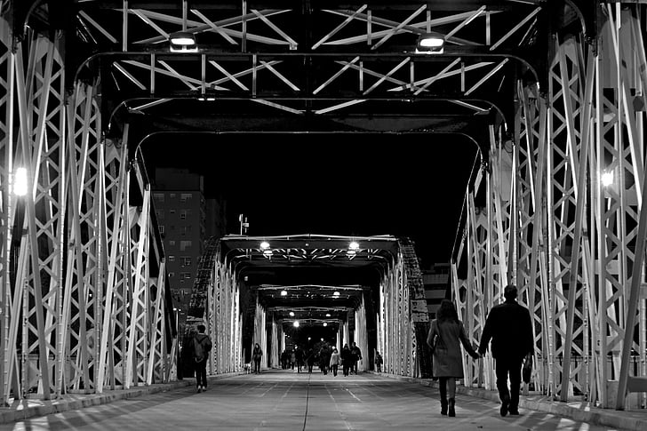 grayscale photo of people walks on steel bridge