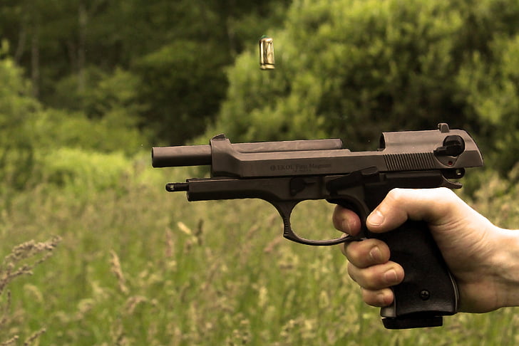 person firing black pistol near green grass field