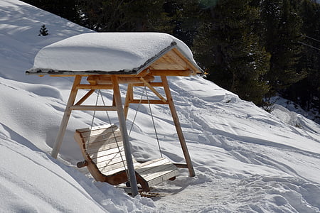 brown wooden swing bench filled with snow