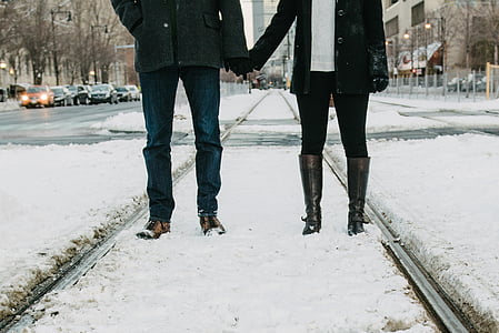 man holding woman wearing jackets standing on railroad during winter