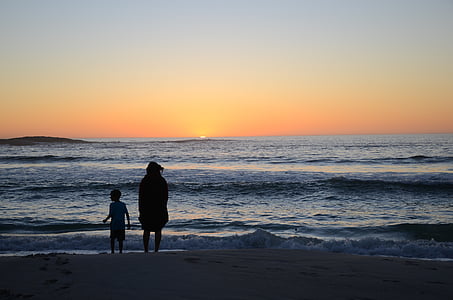 silhouette of child and person standing beside seashore