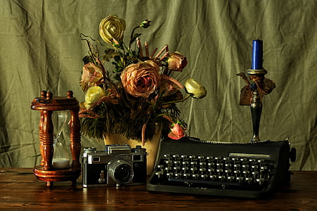 typewriter beside camera, hourglass, flower decor, and candlestick with candle on table
