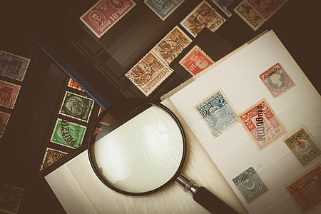 assorted-color postage stamp collection near magnifying glass on table