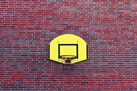 yellow-and-black basketball board and hoop on red-and-black brick wall during daytime