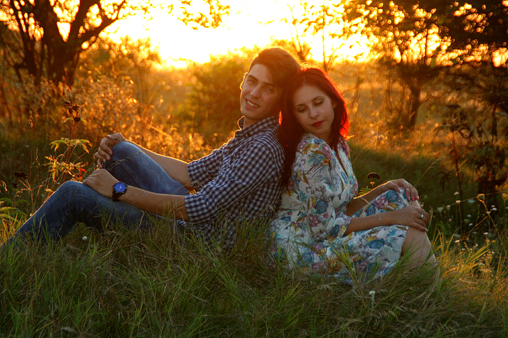 man and woman leaning to each other sitting on grass field during golden hour