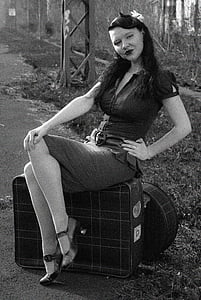grayscale photography of woman wearing mini dress sitting on luggage