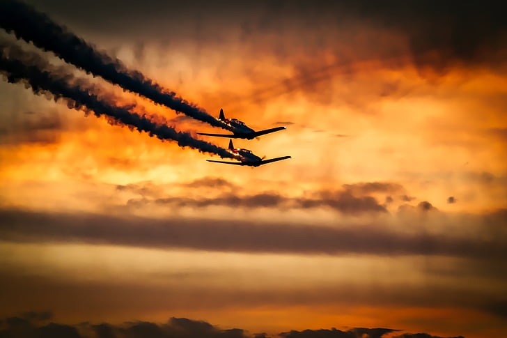 two airplanes flying in the air during sunset