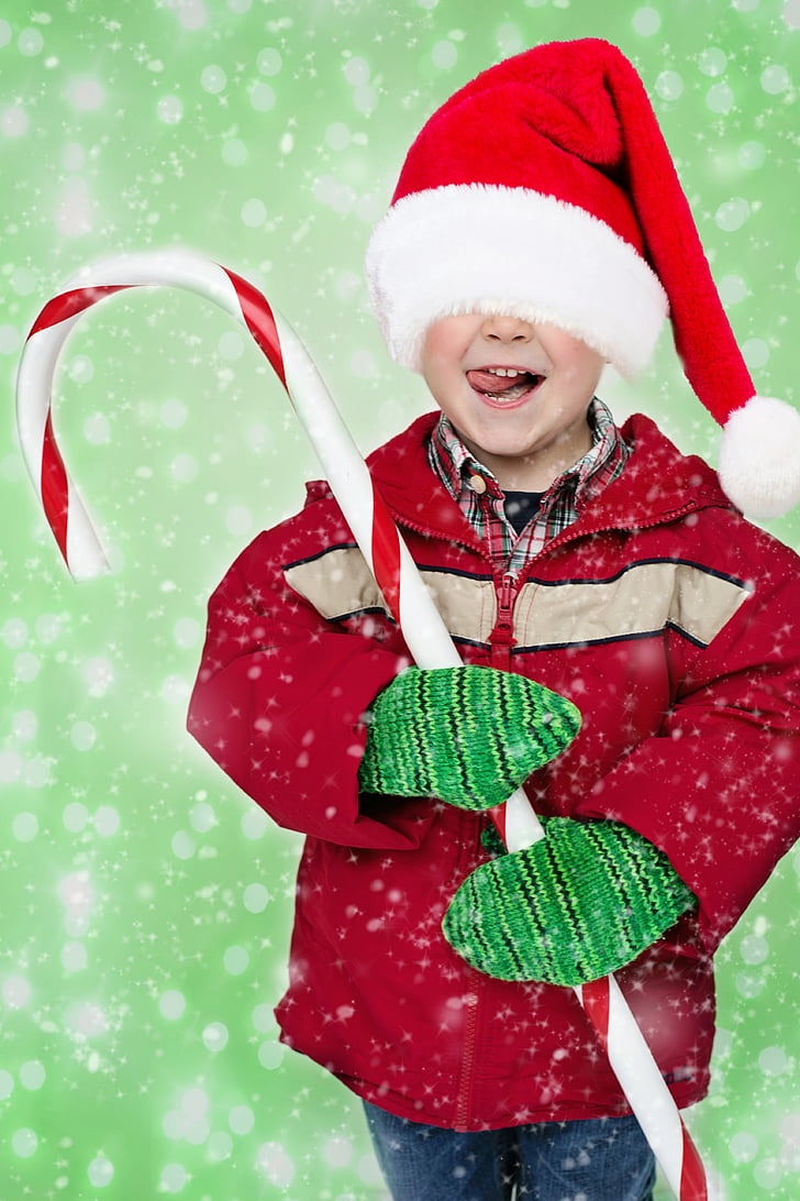 boy in red jacket, red Santa hat and green gloves holding large candy cane
