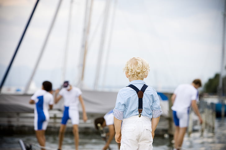 blonde boy wearing blue shirt standing near body of water