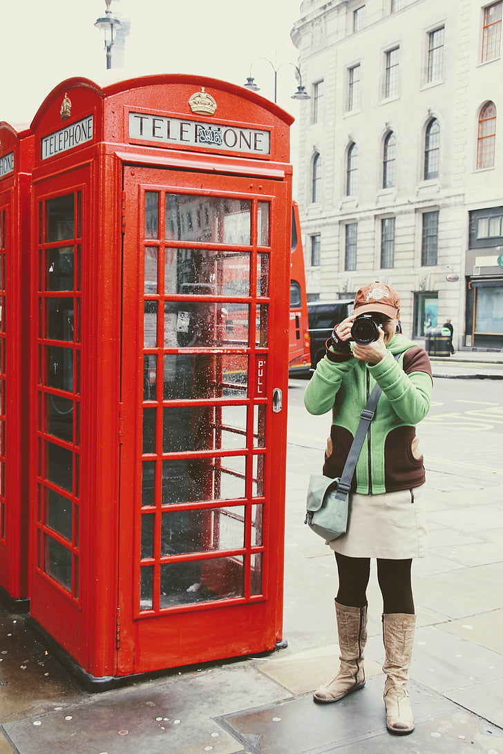 woman holding camera standing near telephone booth